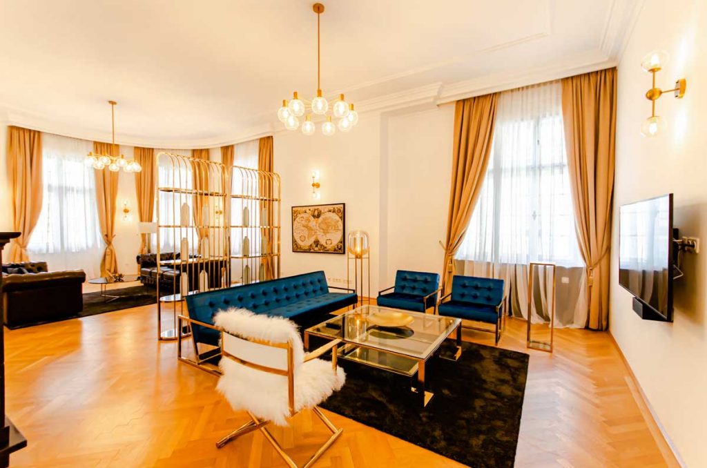 The living room of one of our beautiful furnished 5 room apartment in the 3rd district of vienna. The bold mix of warm gold with daring dark blue tones round off the pure elegance of the high-quality furniture. Relax on one of the Chesterfield sofas in front of the fireplace or listen through the music boxes. 