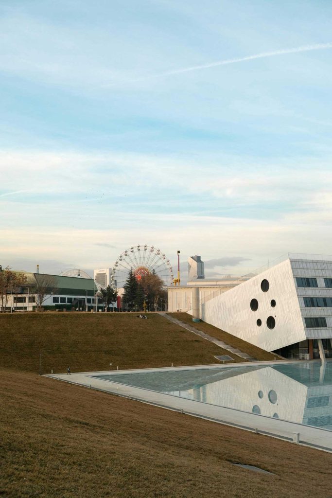 View of the Vienna Prater Ferris wheel and modern architecture with reflective pool at sunset