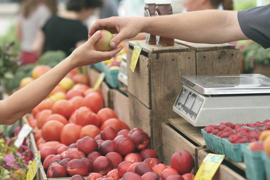 Two people exchanging an apple on a market stand, with frsh fruit in the back, in Viennas 6th district at Naschmarkt - a famous market in Vienna