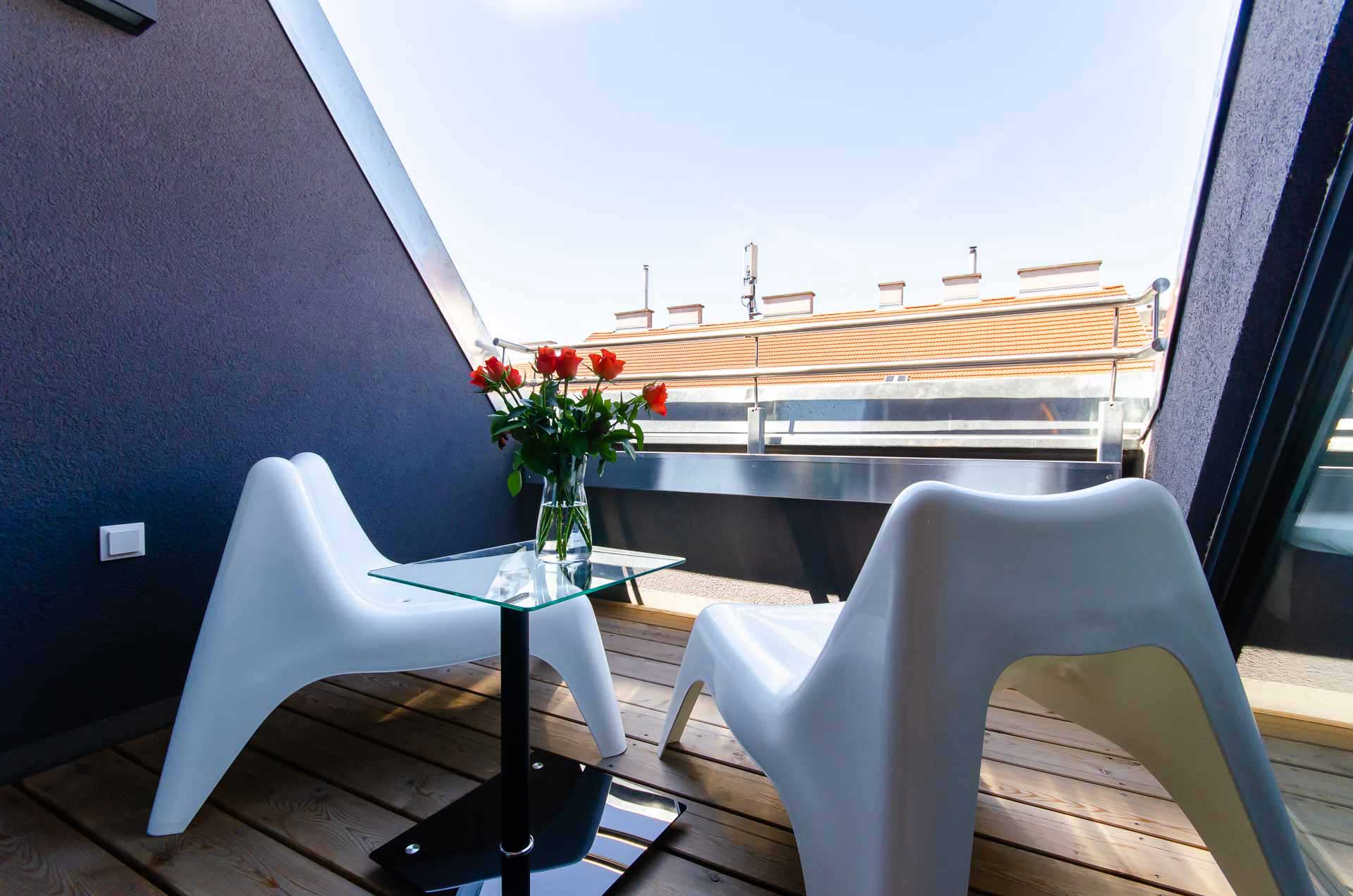 Two white chairs and a small table with charming red roses on it, on a cozy balcony in Vienna