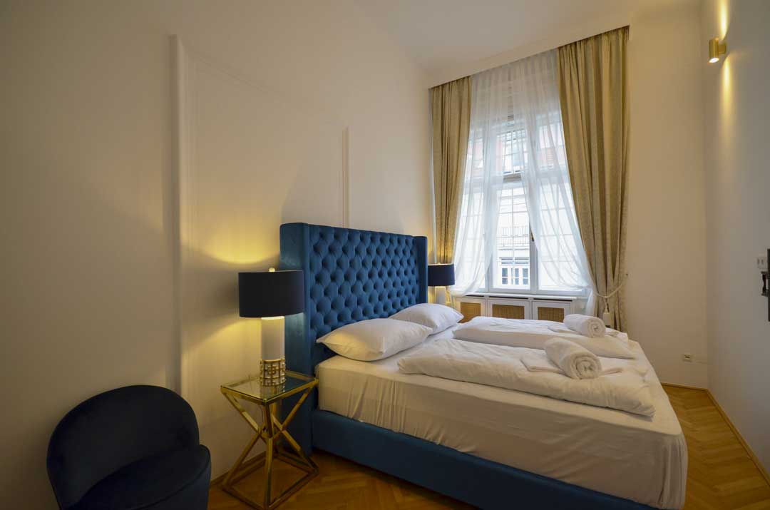 Cozy and blue velvet kingsize bed in a historic room with goden end tables and beautiful lamps on them
