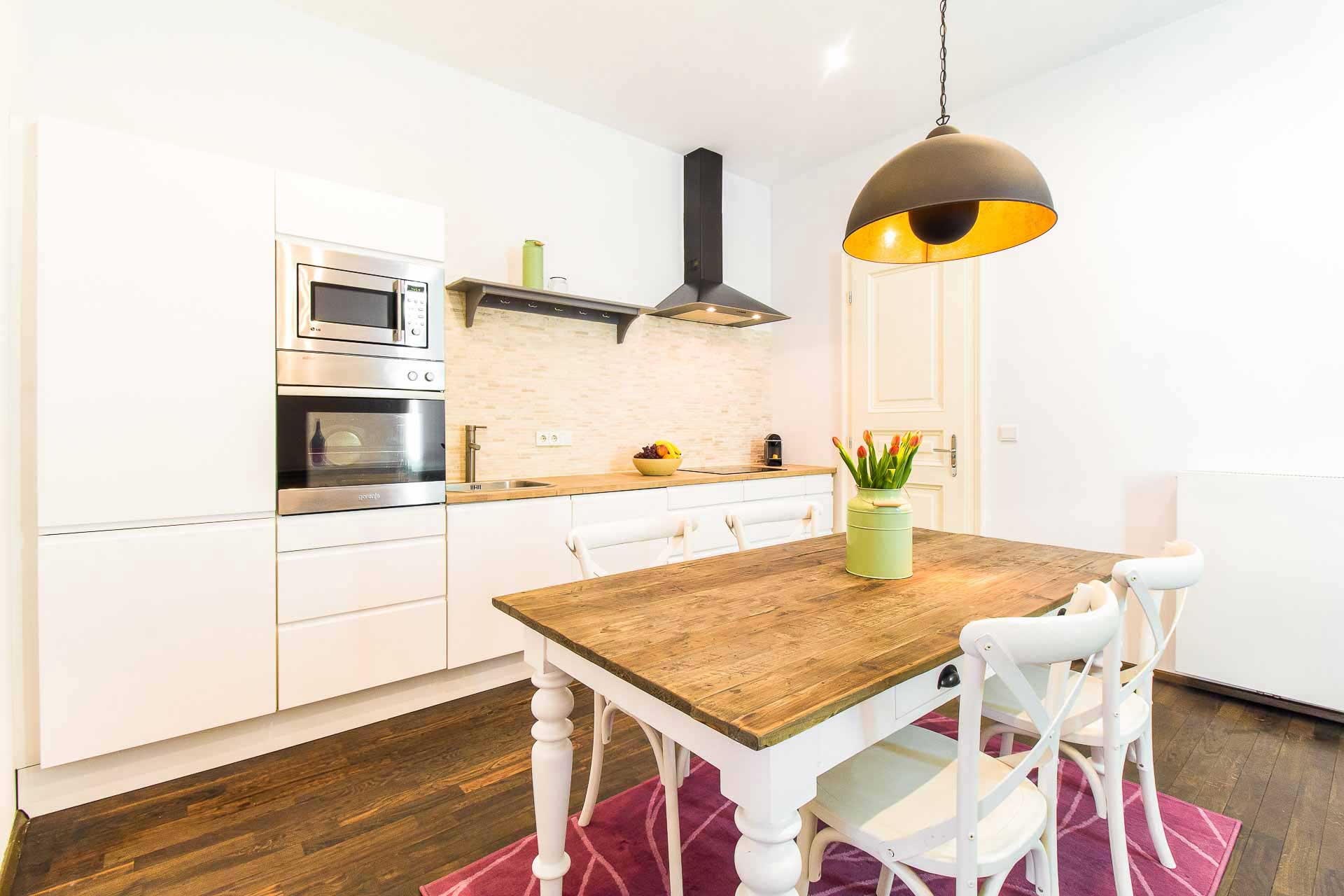 Clean and modern white kitchen with a wooden and white table in front and comfrotable white chairs, on top of the table fresh tulips