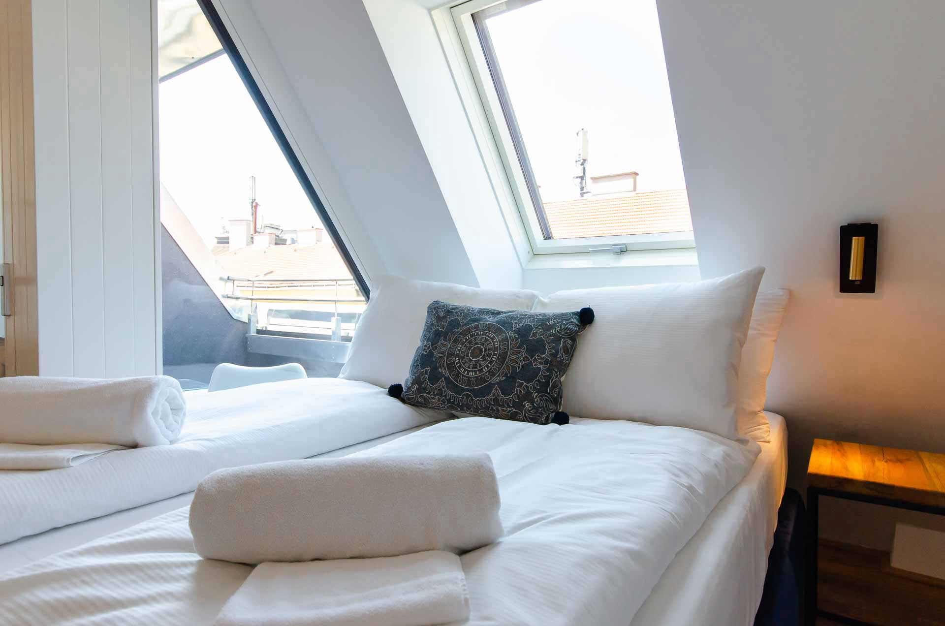 Kingsize bed with fresh linen and towels on top, above a bright skylight