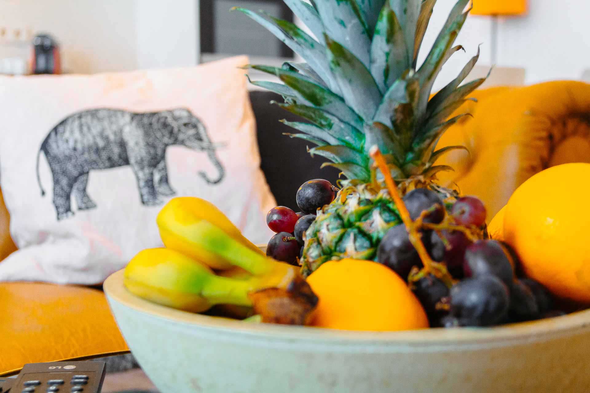 A big bowl with fresh fruit and a cushion with an elephant print on it in the back