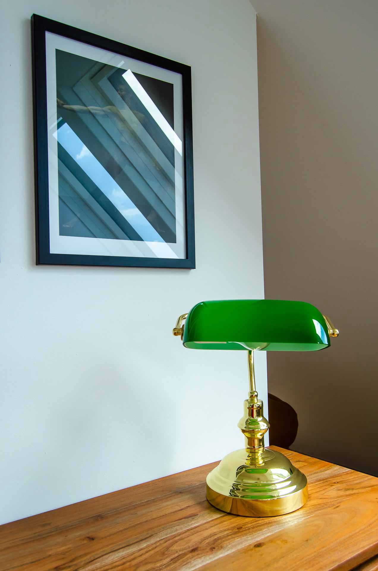 Historic green and gold lamp on wooden table and a photograph on the wall in the back