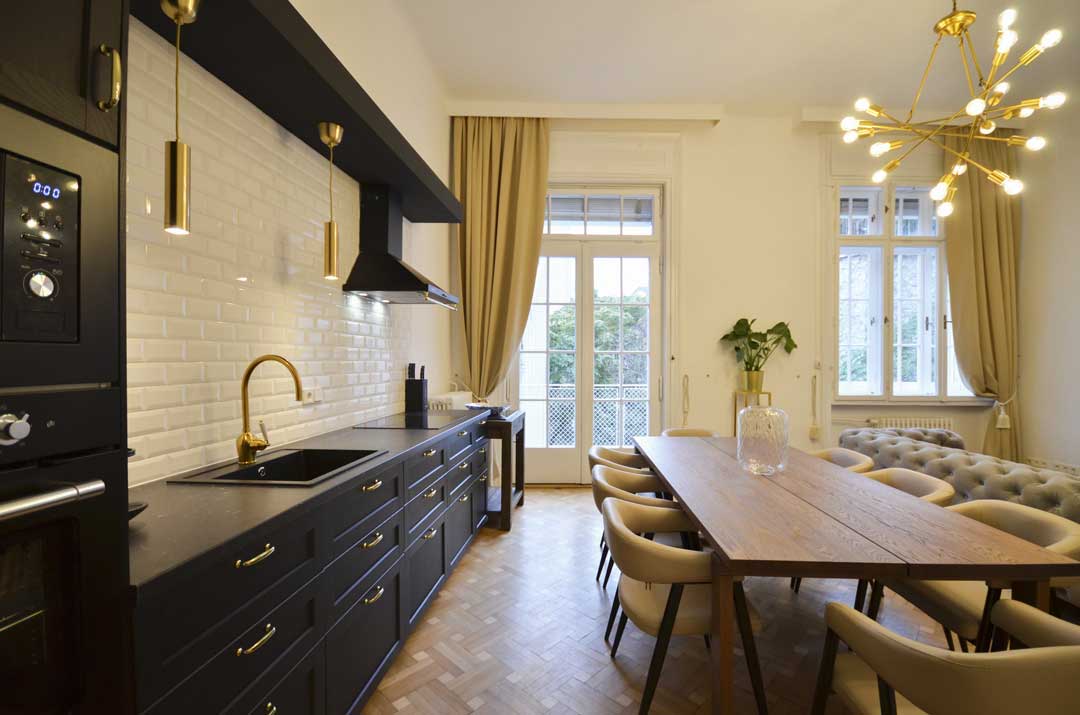 On the left: elegant black kitchen with golden handles , on the right: long wooden table and beige chairs