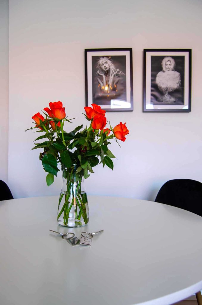Fresh red roses on round white table; 2 black and white photographs on the back wall