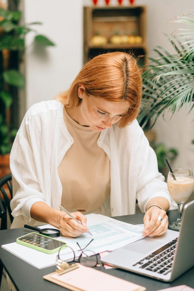 A woman looking at papers, she has a computer in front of her and a calculator
